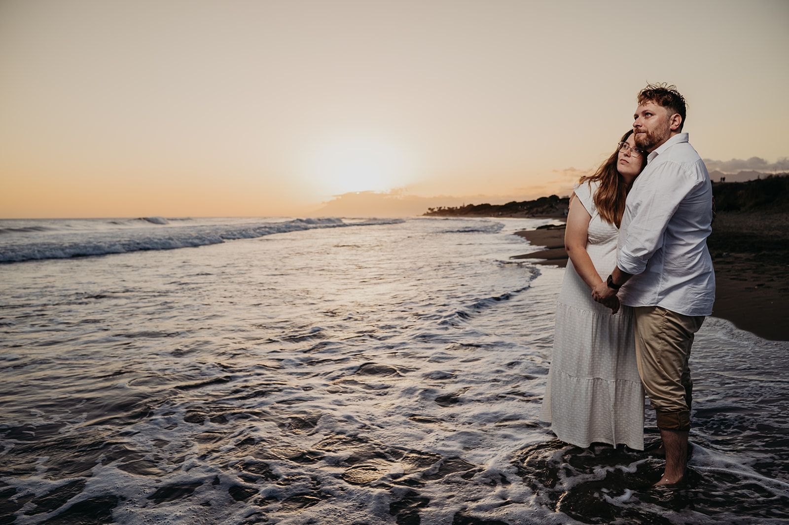 Una pareja abrazándose en la playa al atardecer, con las olas llegando a la orilla