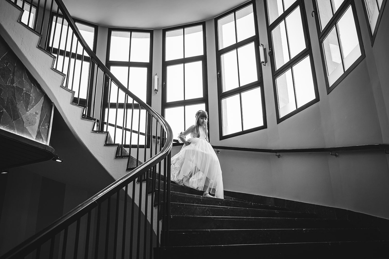 Novia con vestido blanco bajando por una escalera de caracol junto a grandes ventanales
