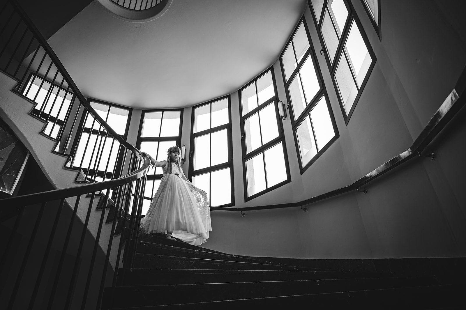 Novia bajando una escalera en un interior luminoso con ventanas curvas