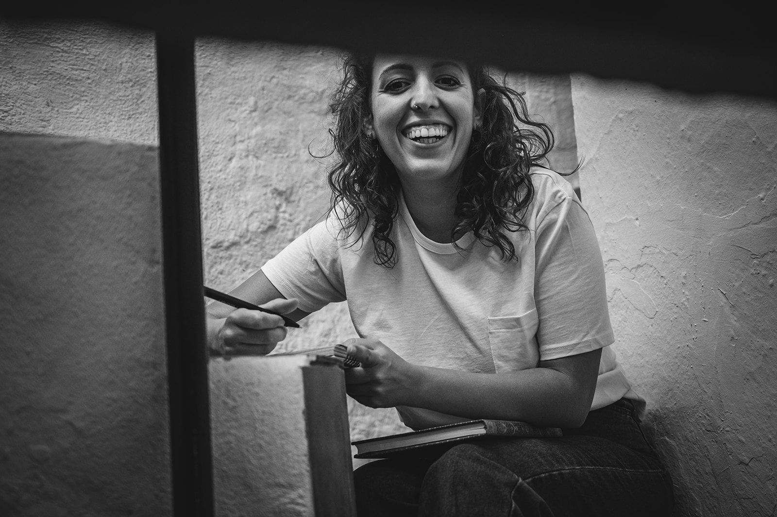 Mujer sonriente sentada en el interior, apoyada en una silla en una foto en blanco y negro