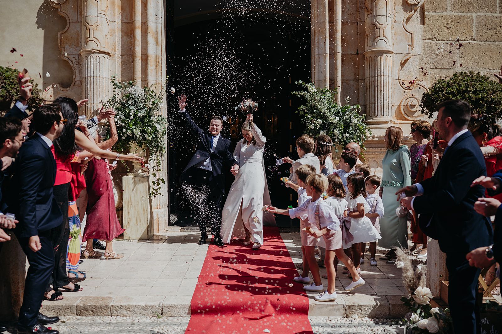 Los novios y sus invitados salen de la iglesia por una alfombra roja mientras los asistentes lanzan confeti