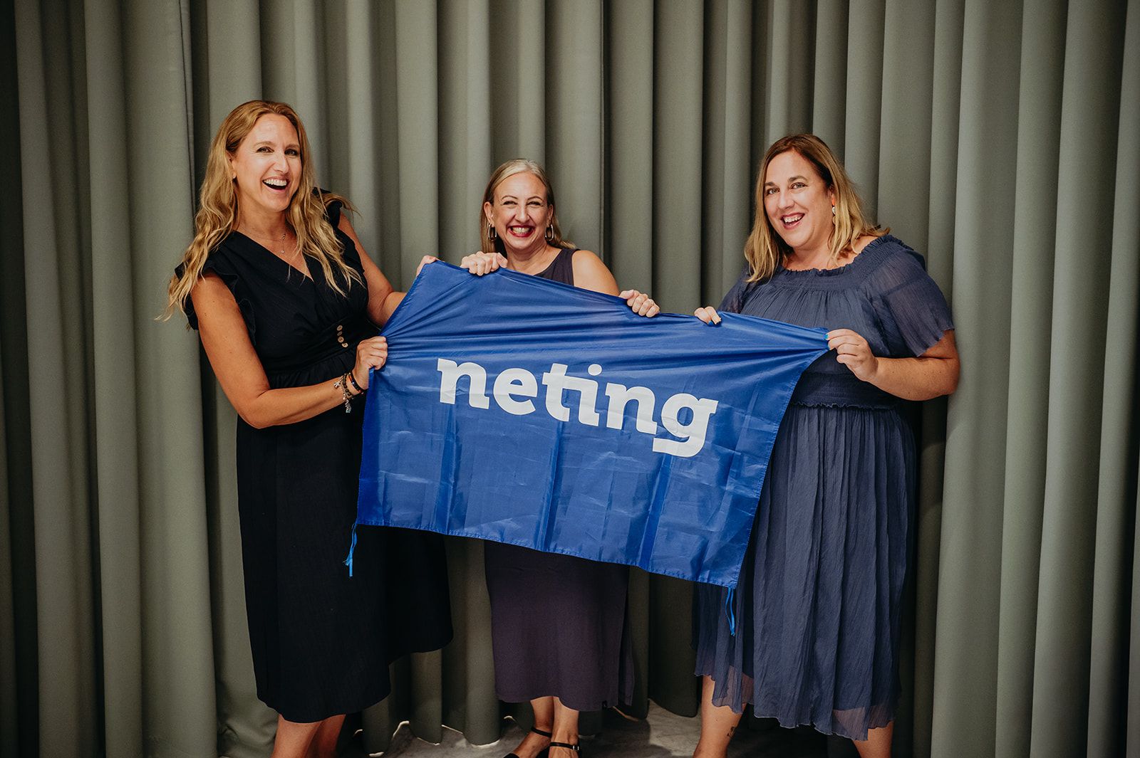 Tres mujeres sosteniendo una pancarta azul de «neting» delante de unas cortinas