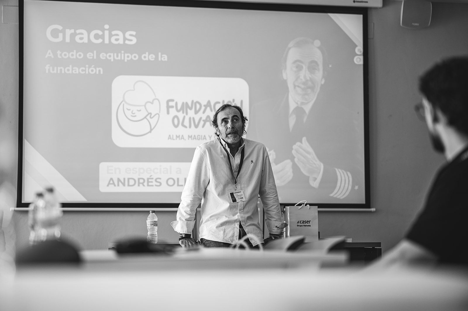 Un orador en un atril presenta en una sala de conferencias, con «Gracias» proyectado en la pantalla detrás de él