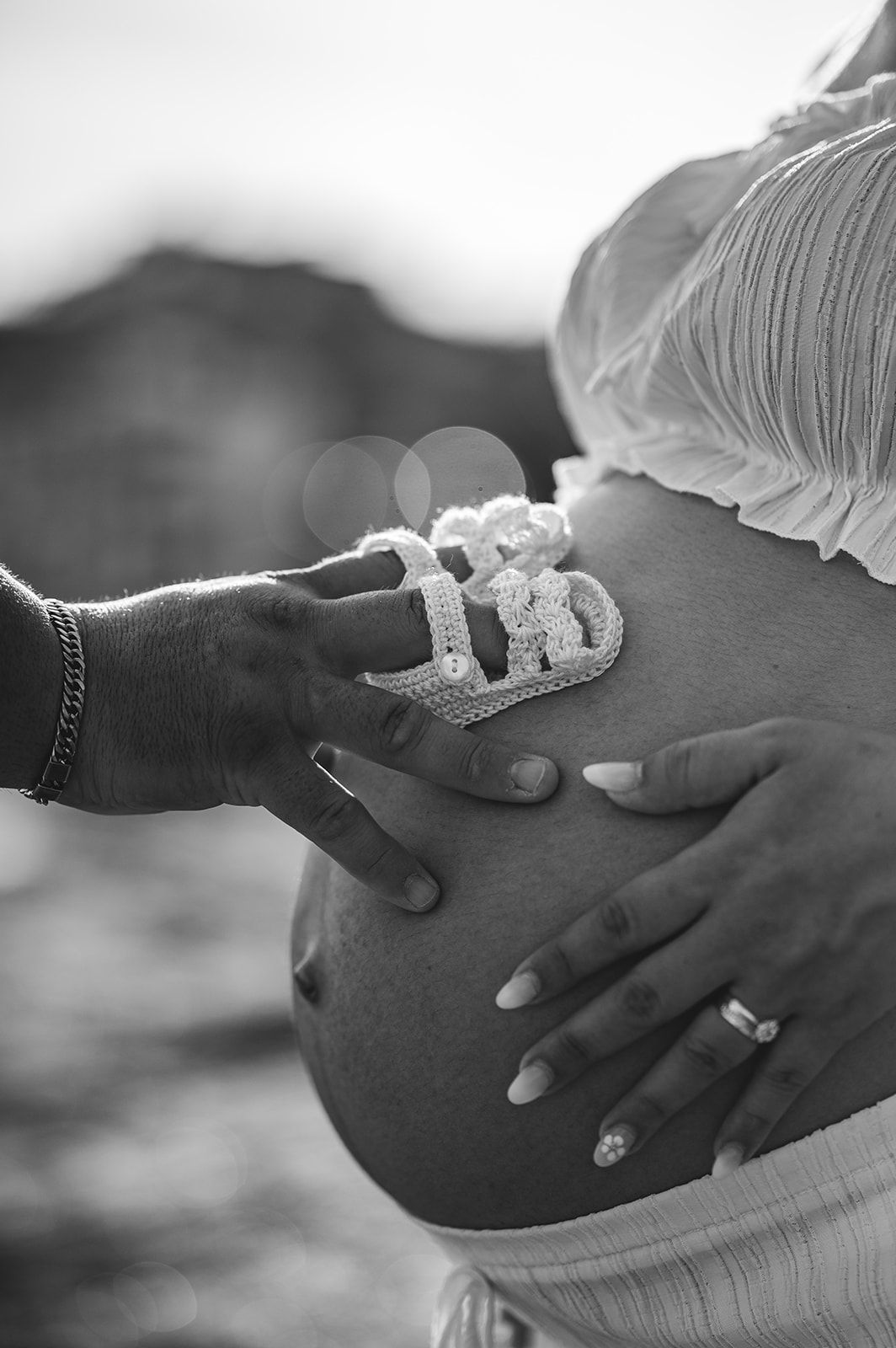 Manos tocando una barriga de embarazada con unos zapatitos de bebé encima, en blanco y negro