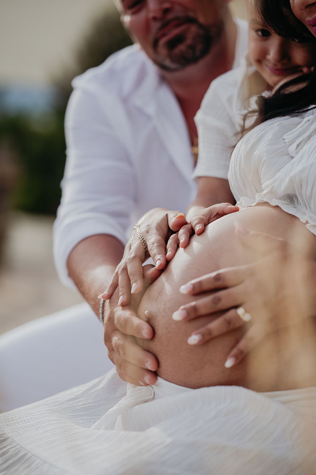 Dos personas vestidas de blanco sostienen suavemente una barriga de embarazada al aire libre