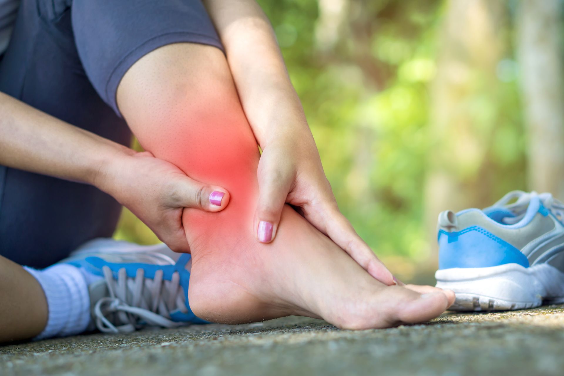 Woman clutching ankle, red area indicating pain, outdoors, sneakers.