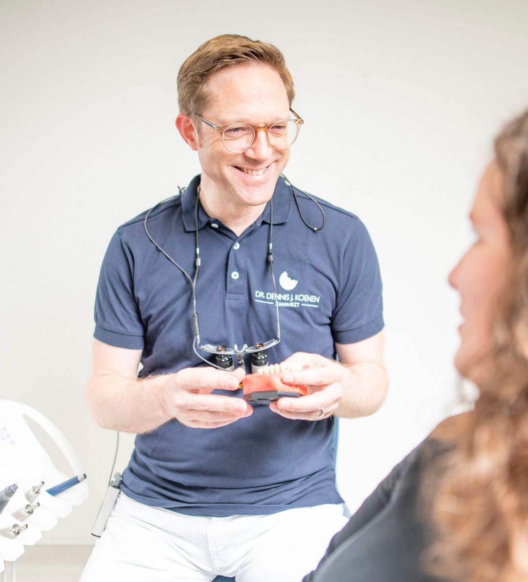 Der Zahnarzt lächelt, während er einem Patienten in einer Zahnarztpraxis ein Zahnmodell zeigt.