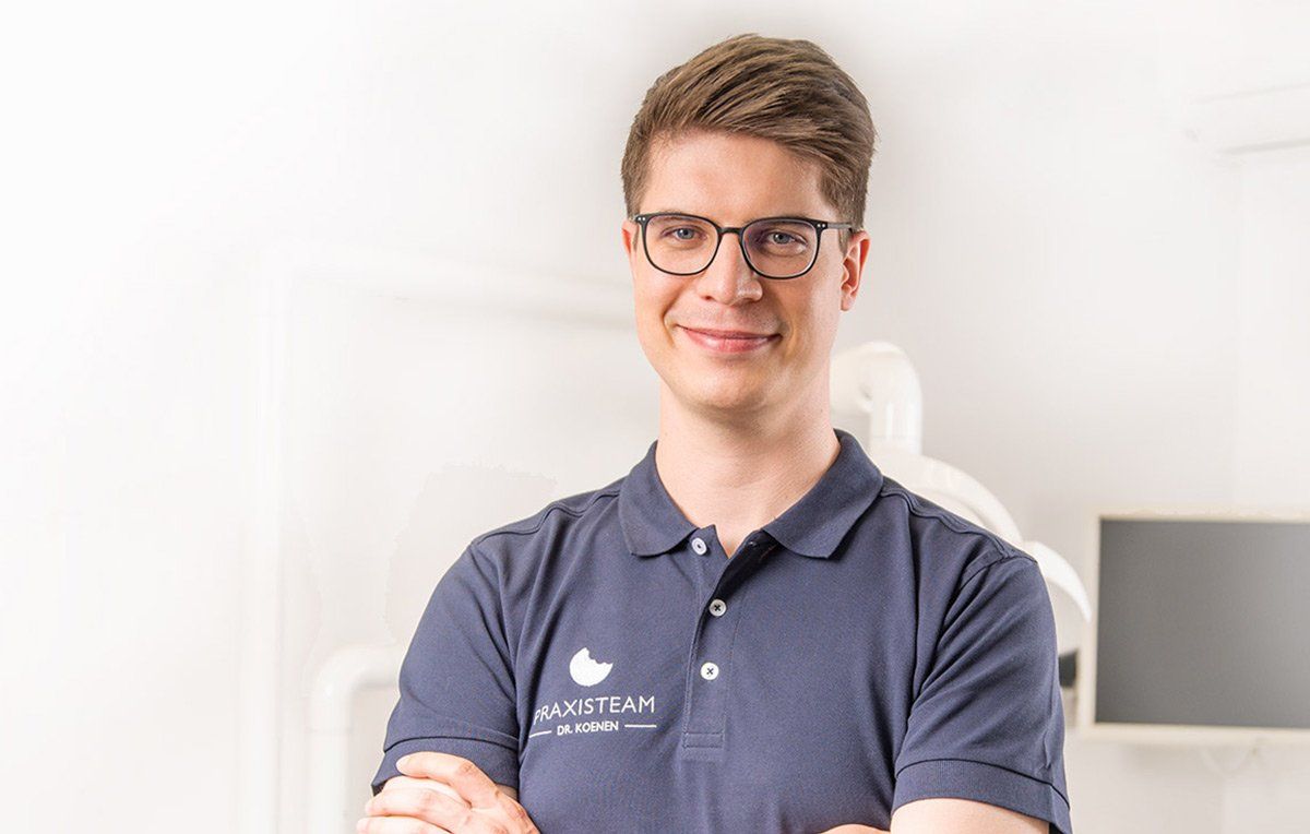 Ein Mann mit Brille und Poloshirt steht mit verschränkten Armen da.