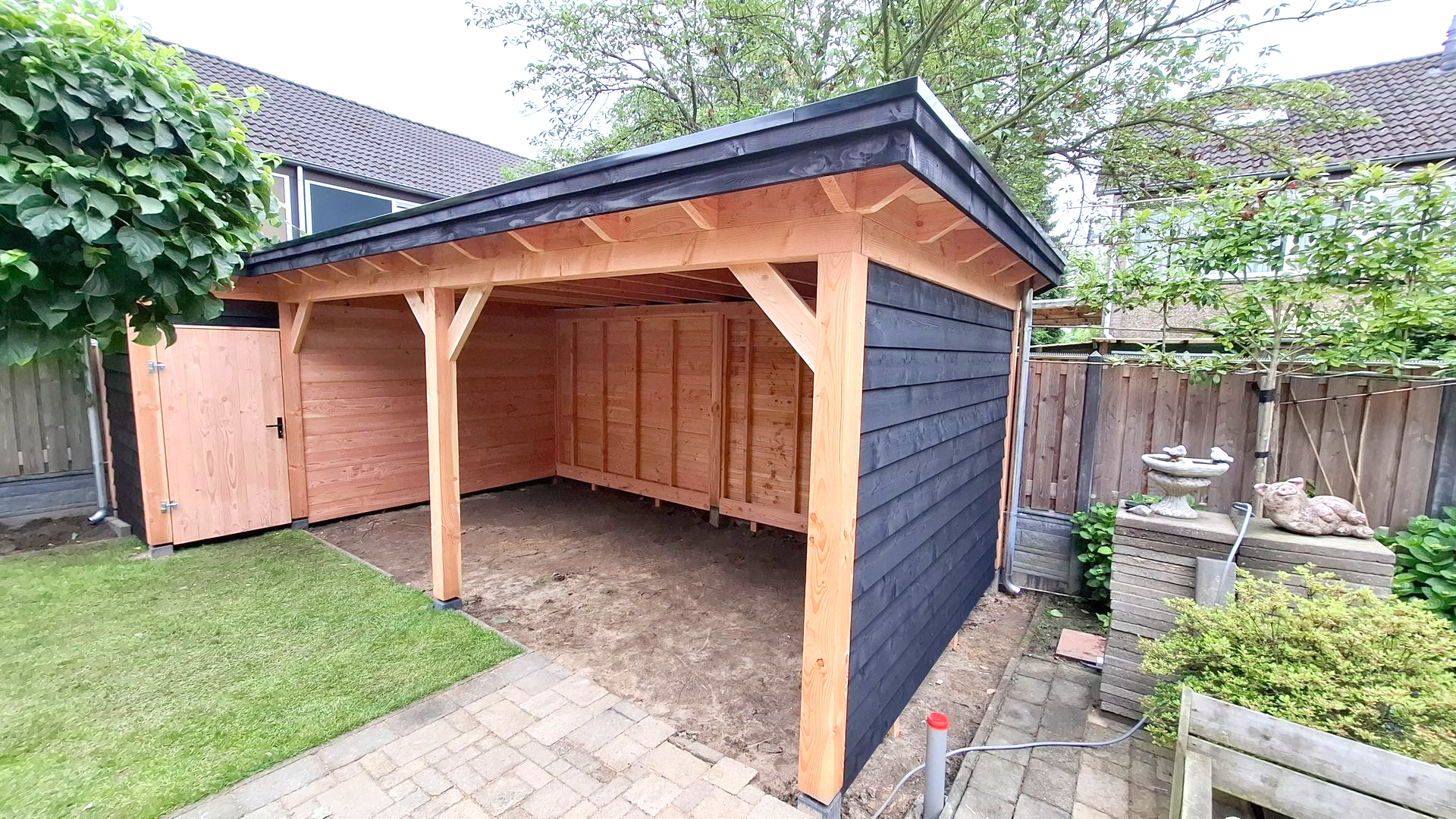 Houten schuur met zwarte gevelbekleding, aan één zijde open, op een terras.