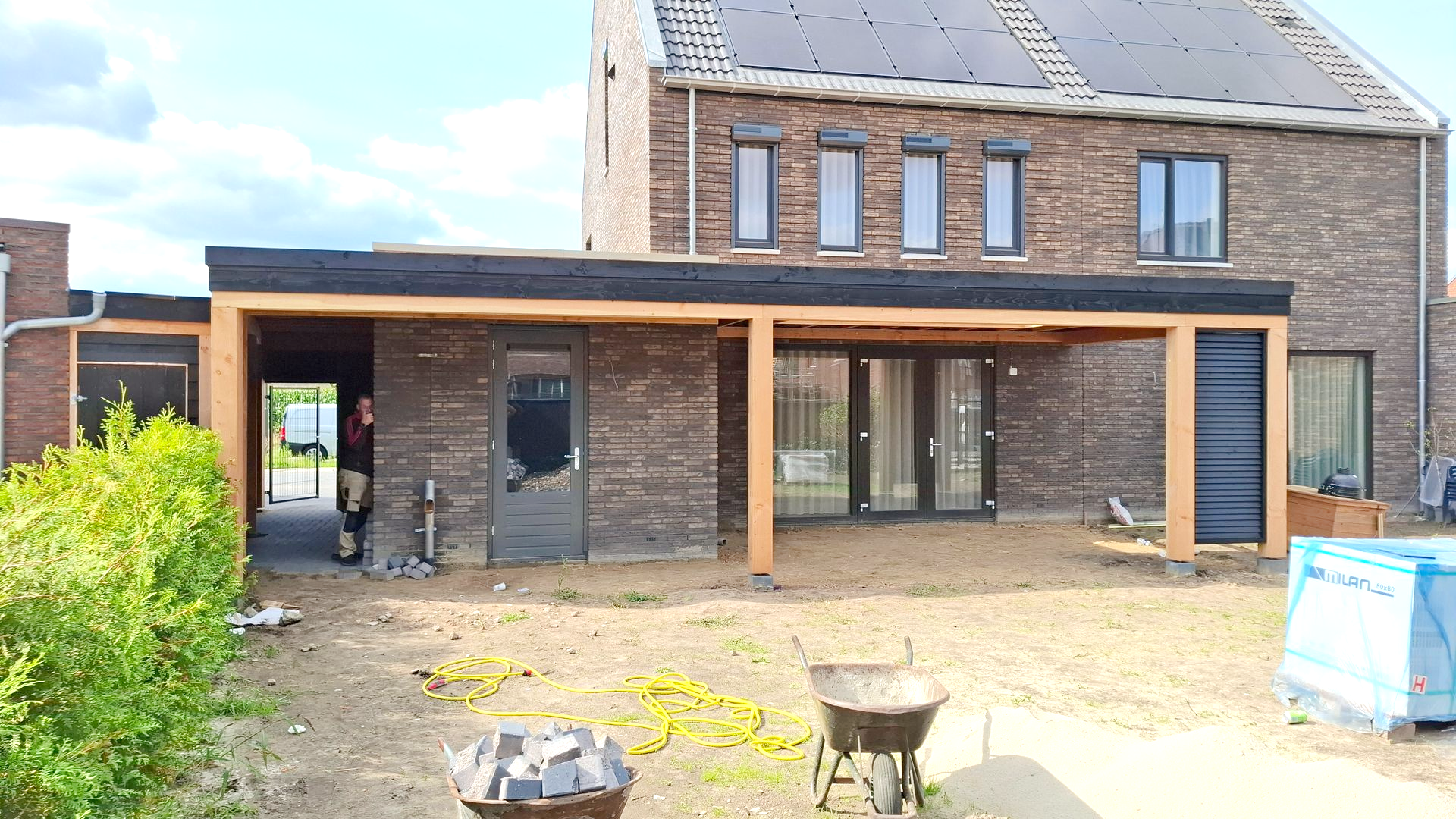 Aanbouw van een terrasuitbreiding in de achtertuin, bruin bakstenen huis, houten frame, onverharde tuin.