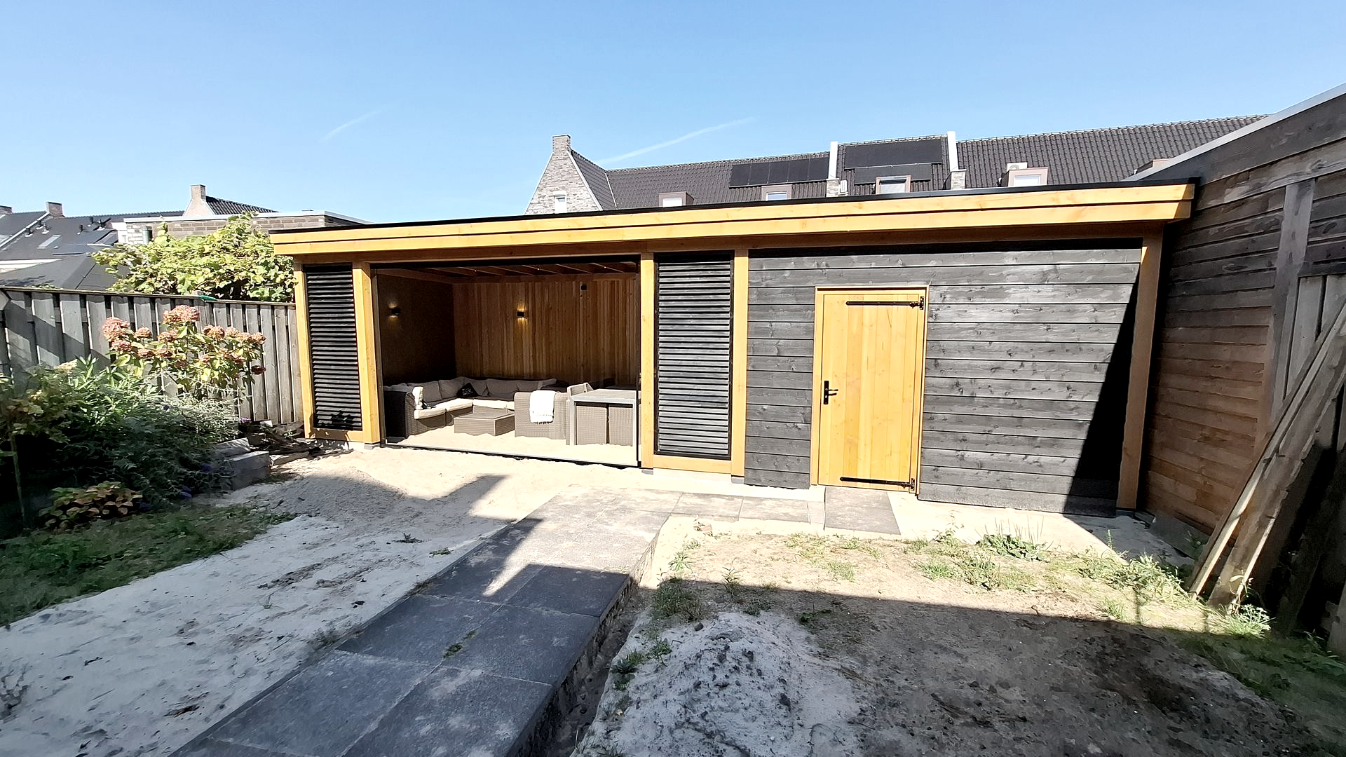 Tuinschuur met een houten dak en zwarte gevelbekleding; rechts bevindt zich een gele deur.