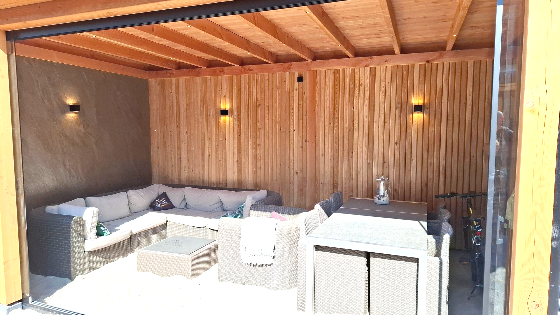 Buitenpatio met houten wanden, zitgedeelte, eettafel en schuifdeuren van glas.