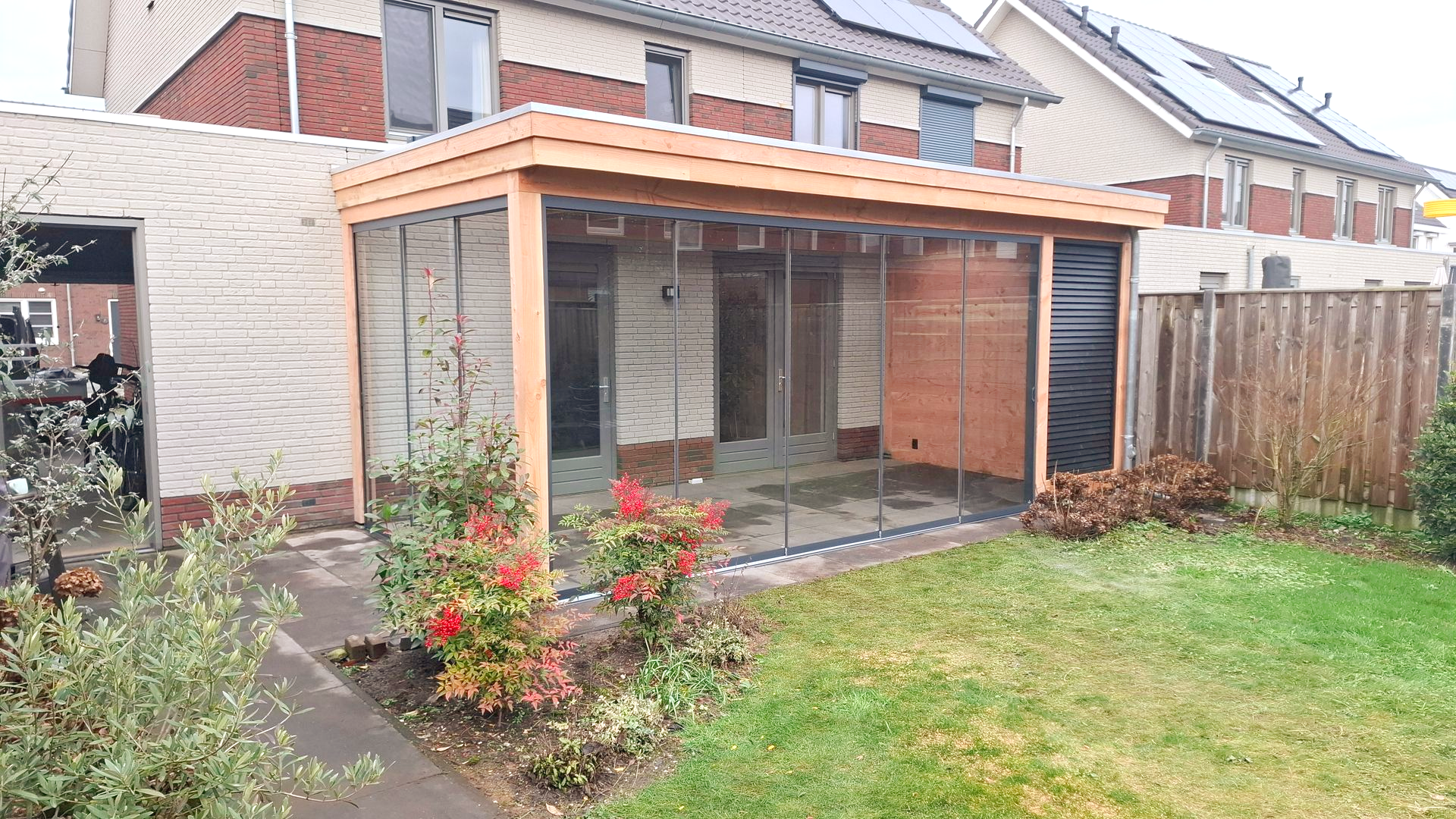 Houten terrasoverkapping met transparante schermen, bakstenen muur en tuin.