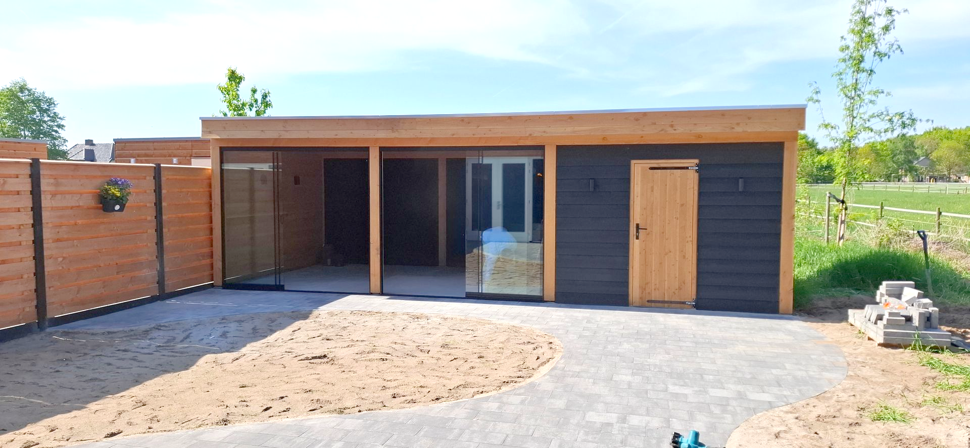 Een modern houten gebouw met een patio, een houten deur en een lichtblauwe lucht.