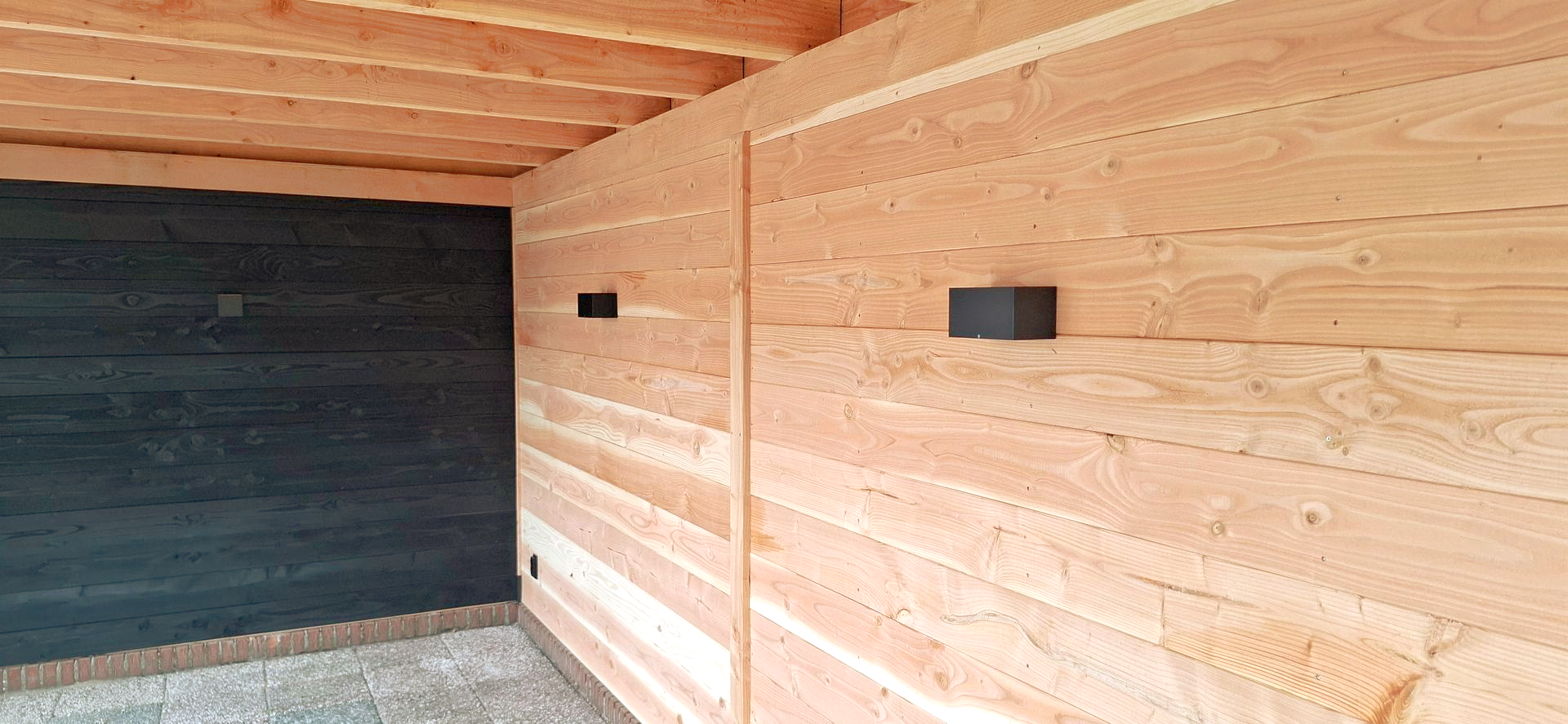 Houten wanden met twee zwarte rechthoekige lampen. Zwarte muur op de achtergrond, houten plafond.
