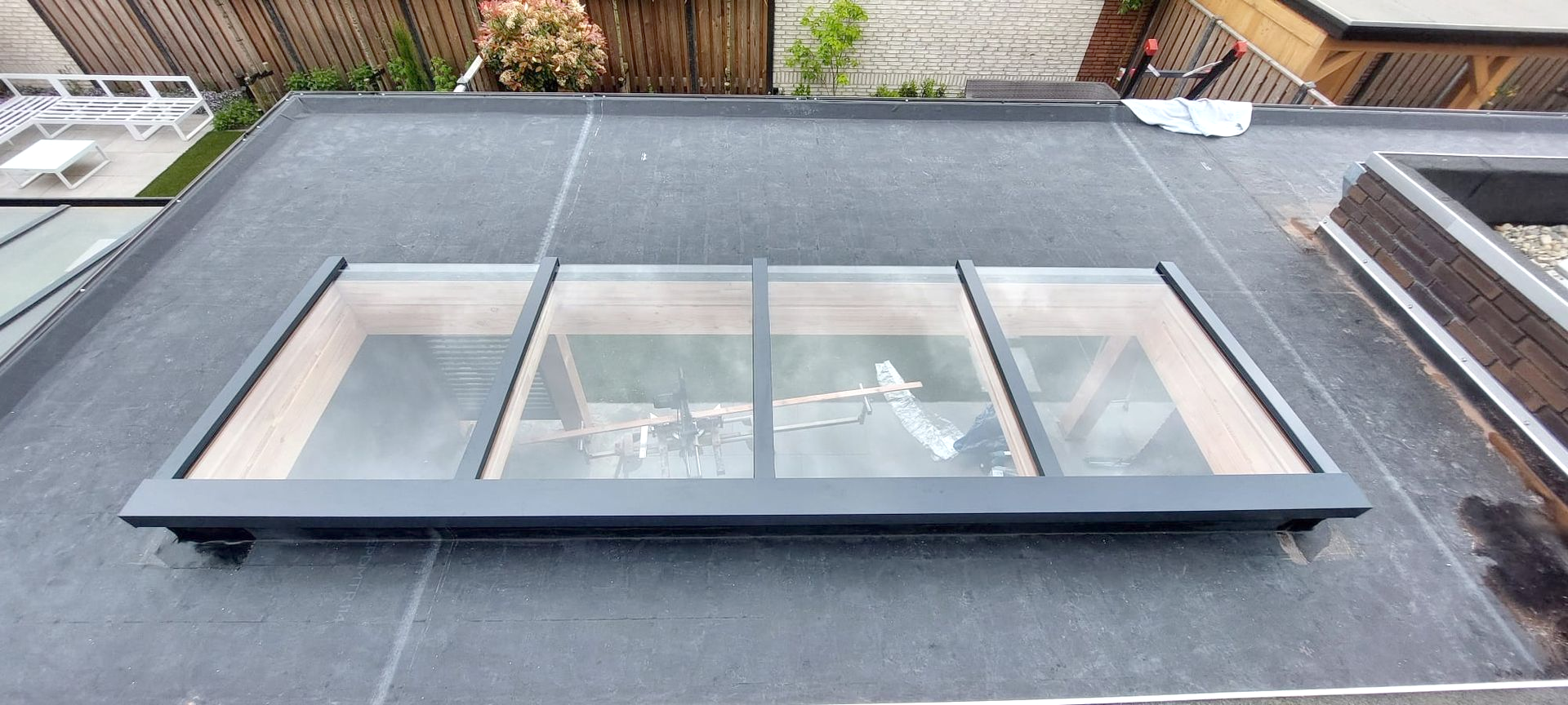 Dakraam in een plat dak. Zwart asfalt dak met een rechthoekig glazen dakraam en een donkergrijs frame.