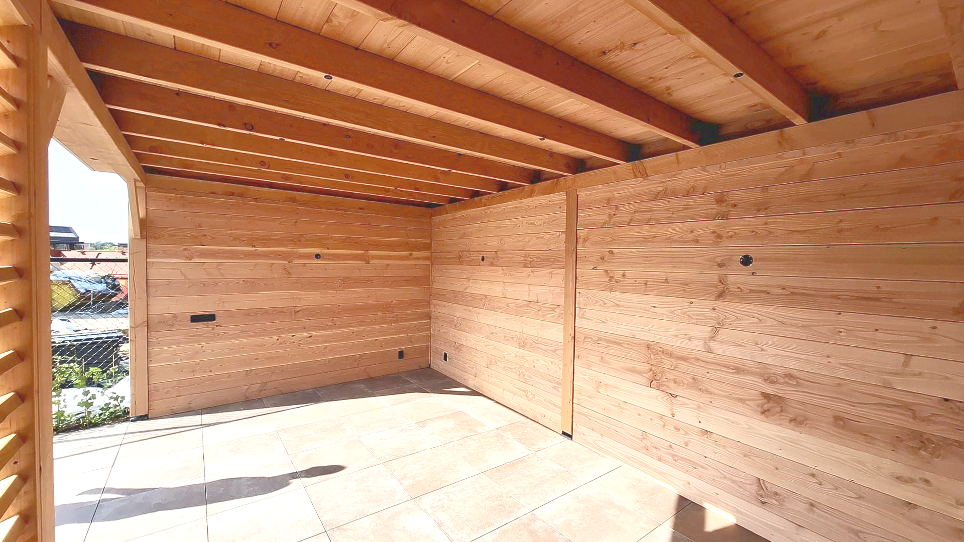 Een buitenconstructie met houten wanden, een plafond van houten planken en een stenen vloer, met uitzicht over de stad.