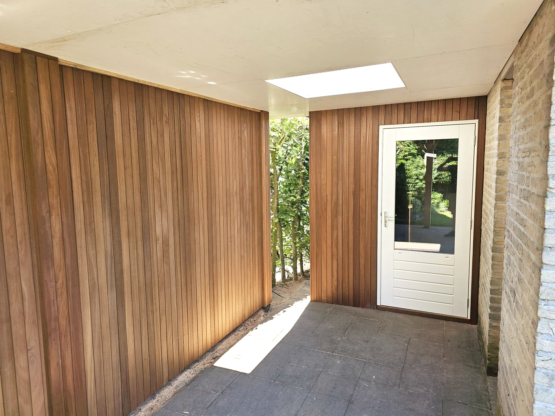 Overdekte loopbrug met houten bekleding en een witte deur, met daarboven een dakraam.