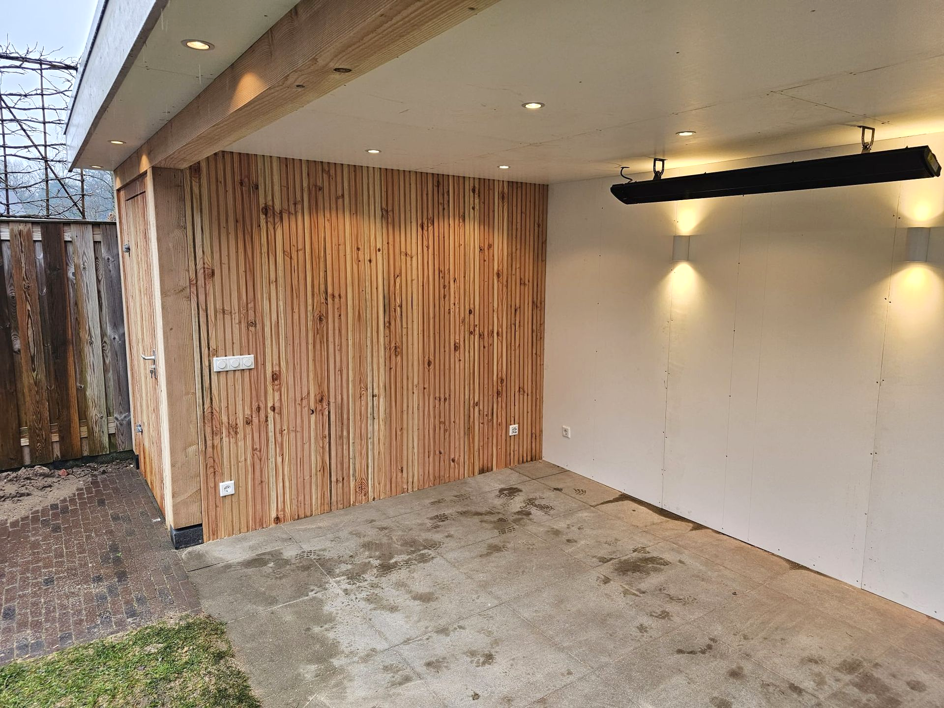 Buitenconstructie met houten lambrisering, betonnen vloer, witte muren en inbouwverlichting.
