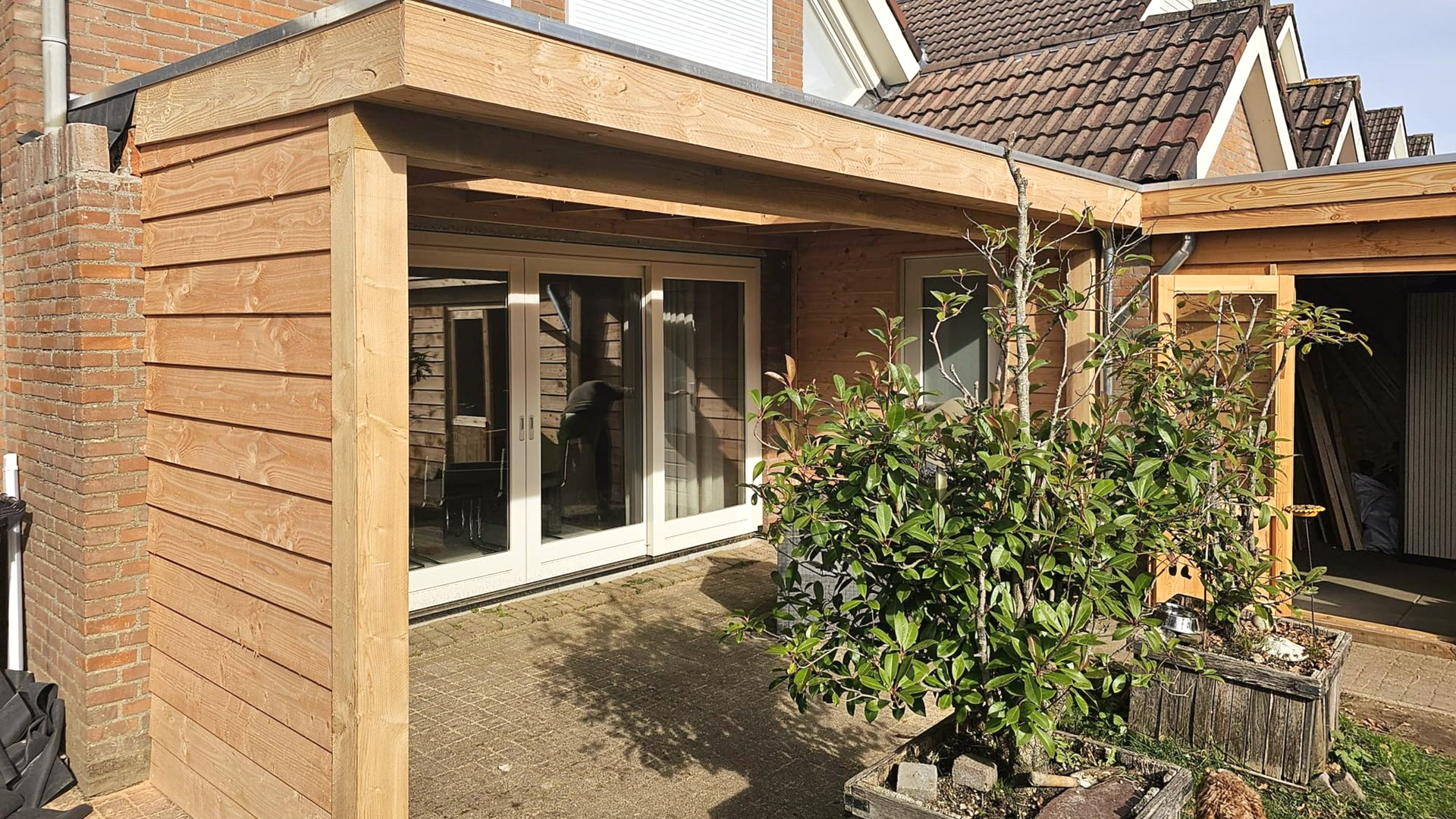 Houten veranda-aanbouw met glazen deuren en een rode bakstenen muur.