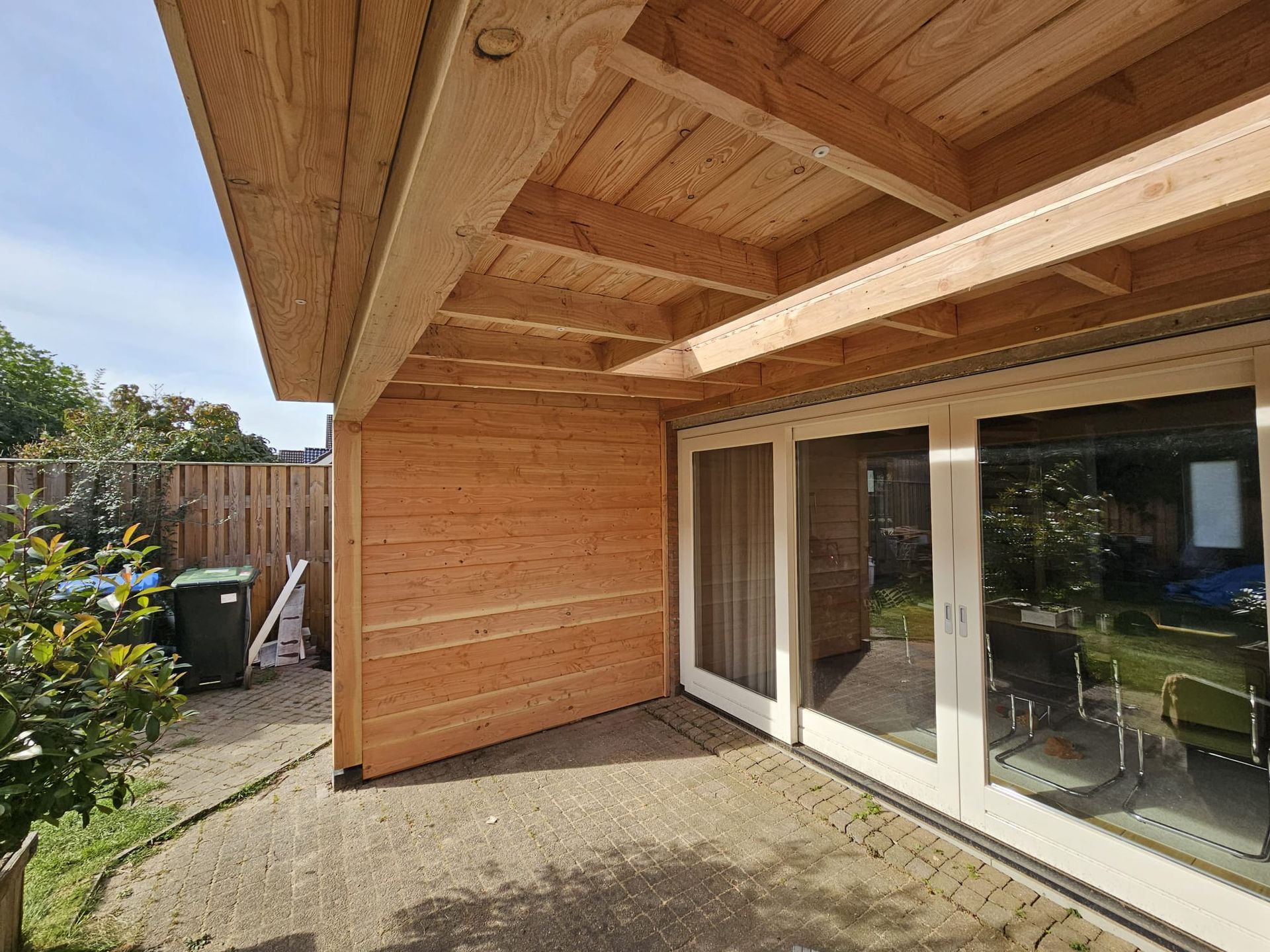 Houten terras met schuifdeuren van glas, een zijmuur en een aangrenzende tuin.