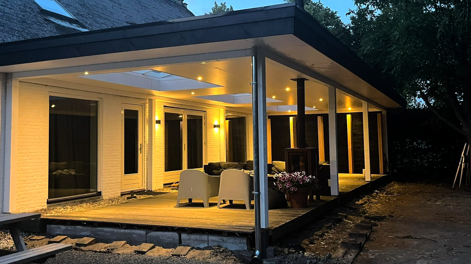 Verlichte patio met witte muren, zwart dak en zitgelegenheid. Avondsetting.
