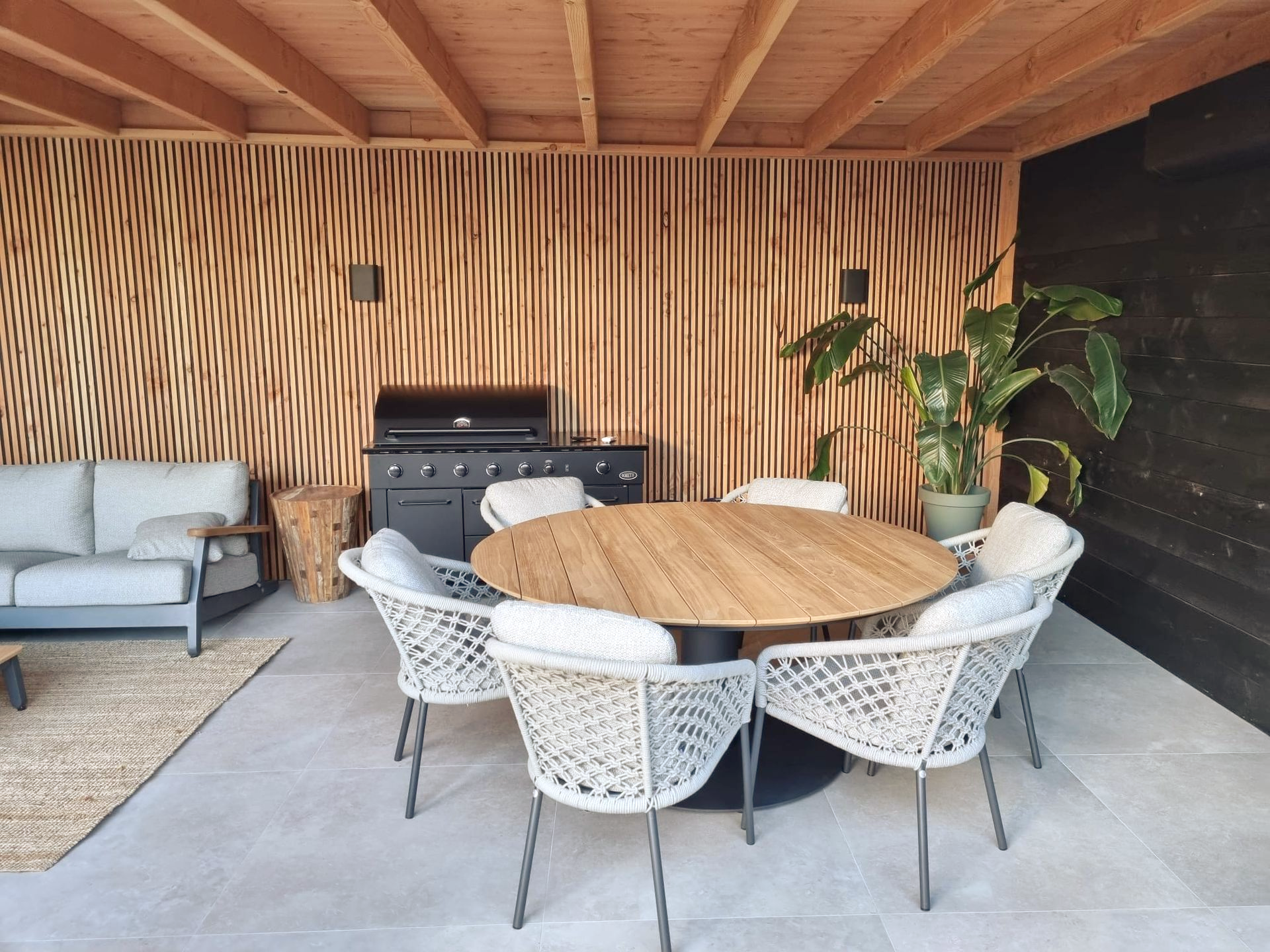 Eetgedeelte buiten met wanden en plafond van houten latten, een ronde tafel en witte stoelen.