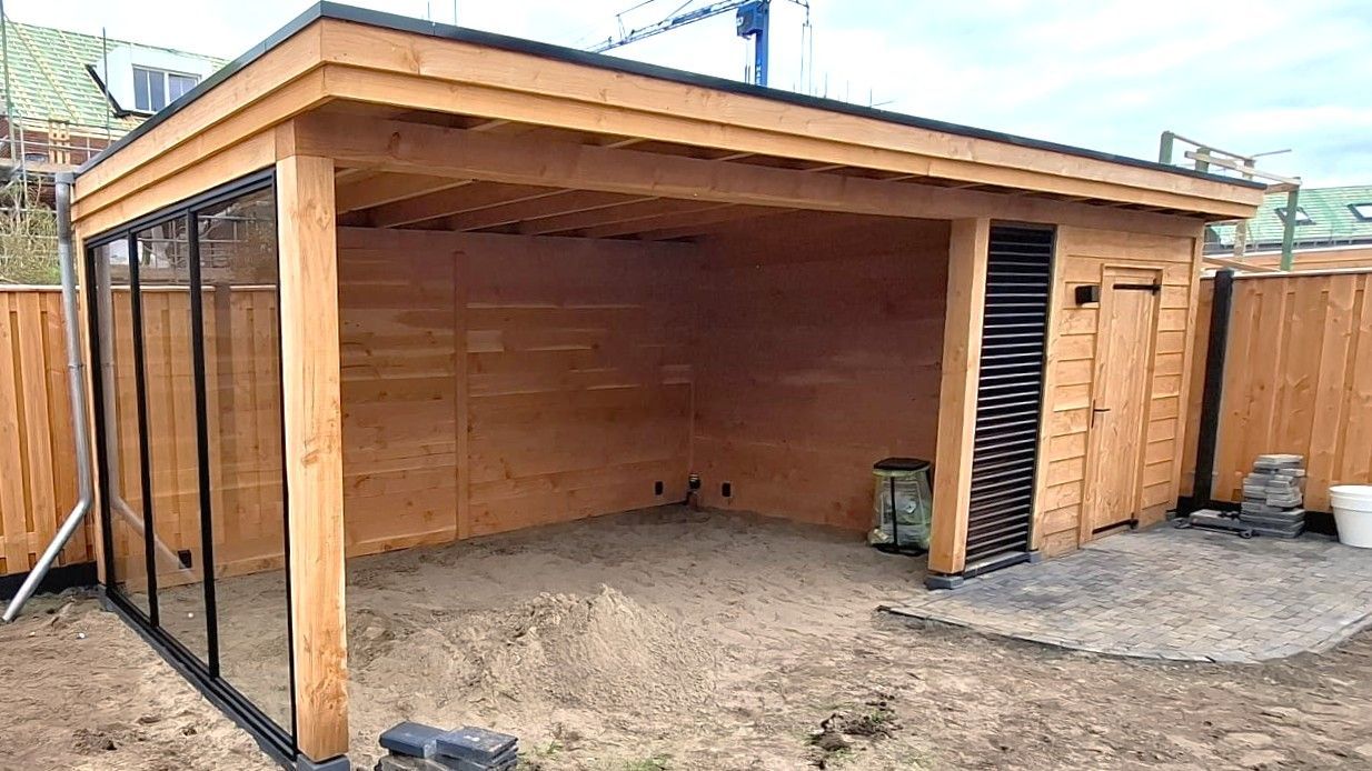 Houten schuur met grindvloer, glazen wand met zwart frame aan de linkerkant, gesloten houten deur aan de rechterkant.