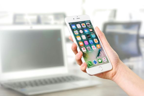 Een persoon houdt een mobiele telefoon vast voor een laptop.