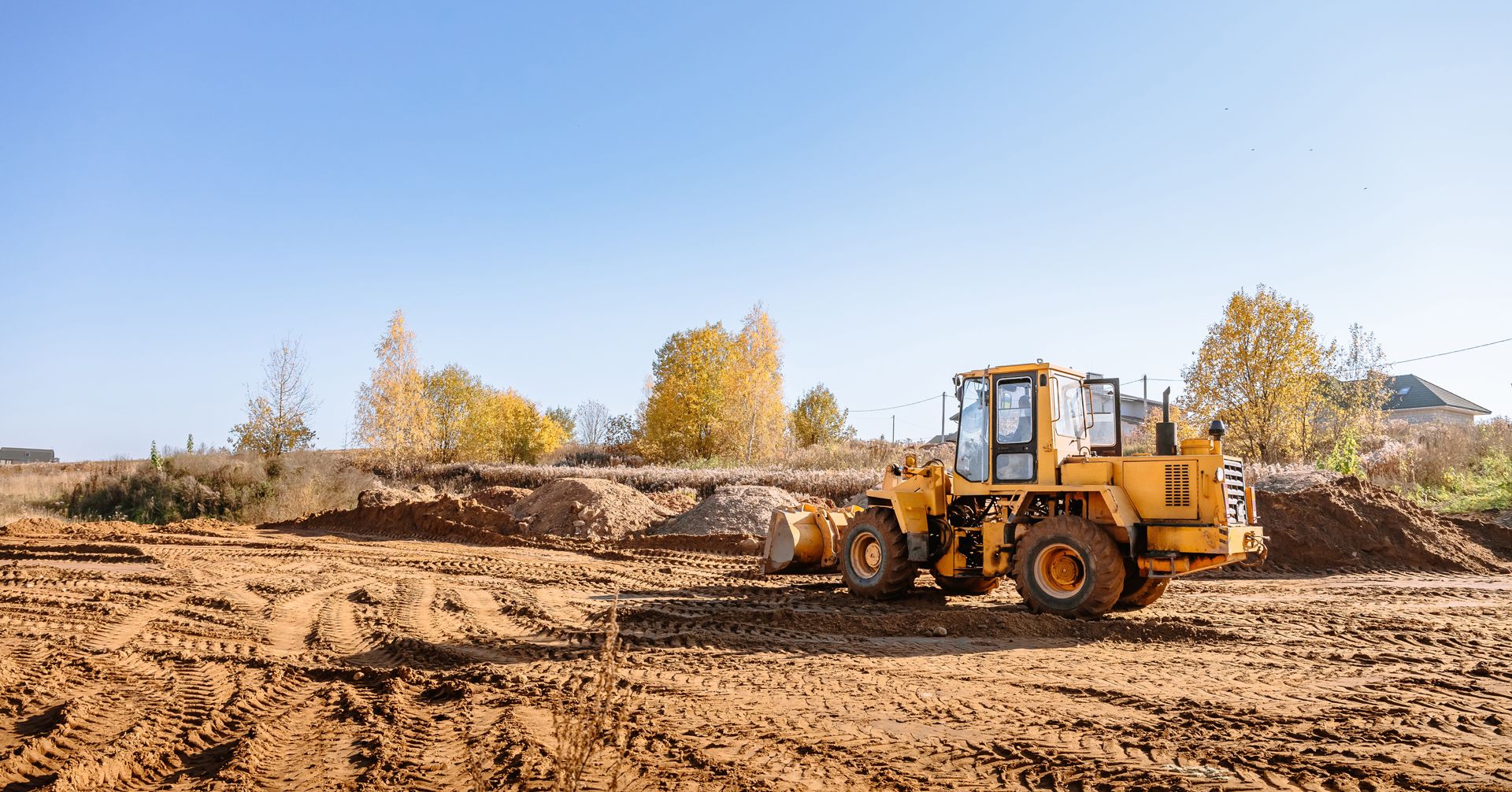 Yellow construction loader on a leveled dirt lot with trees and blue sky in the background.