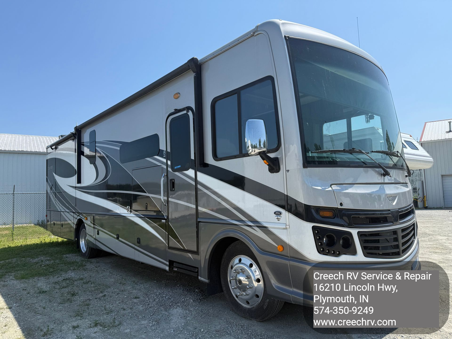 Gray and white RV parked outdoors on a sunny day.