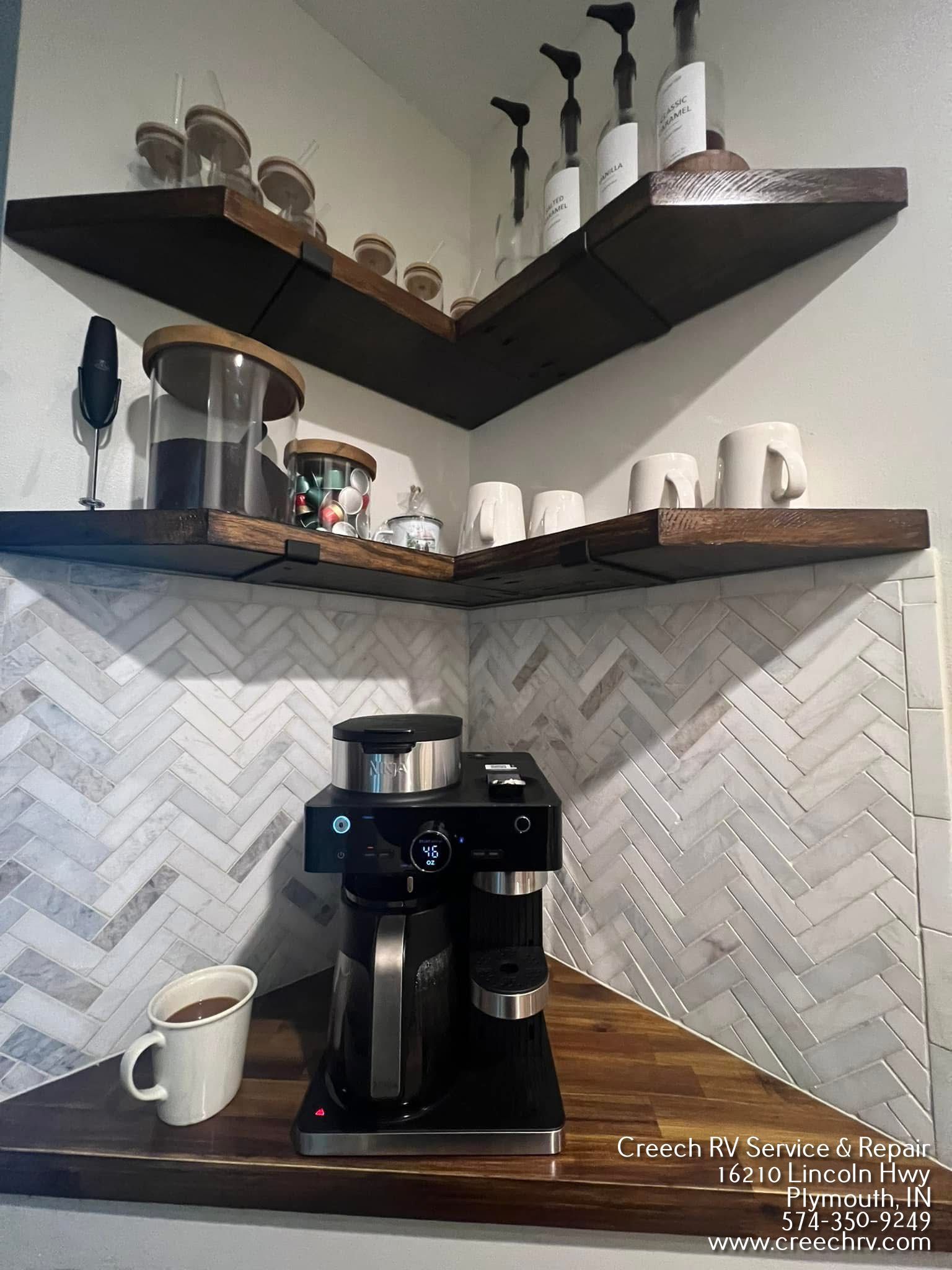 Coffee station with espresso machine, mugs, and supplies on wooden shelves in a corner.