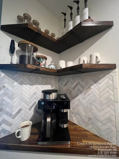 Coffee station in a corner, with shelves, coffee maker, mugs, and a milk container on the counter.