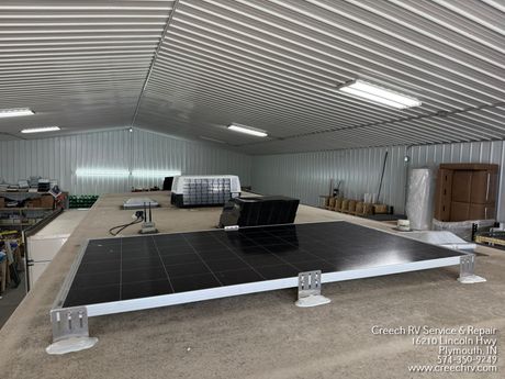 Indoor industrial room with a large black solar panel array on support stands under a corrugated ceiling