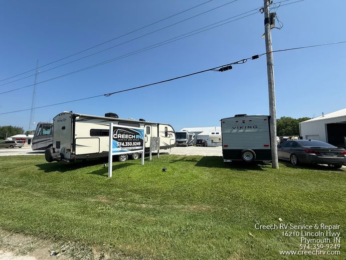 RVs and trailers parked on a grassy lot beside a road under a clear blue sky.