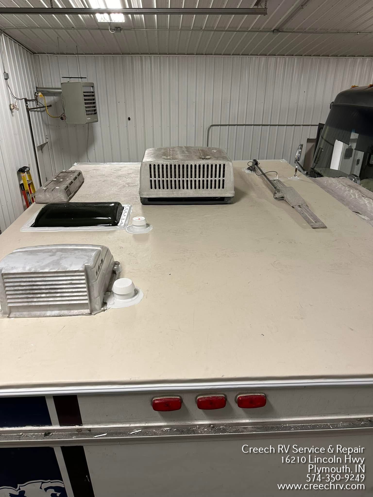 RV roof with air conditioner, vents, and sealant in a repair shop.