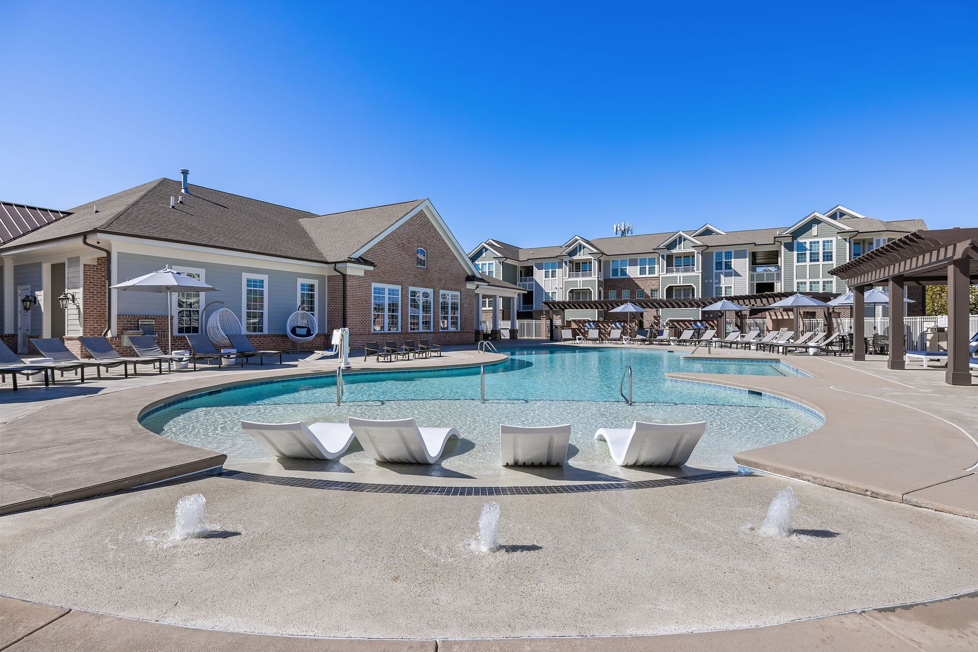 A large swimming pool with a fountain in the middle of it in front of a building at Marquis Ellis Crossing offers apartments for rent in Durham, NC.