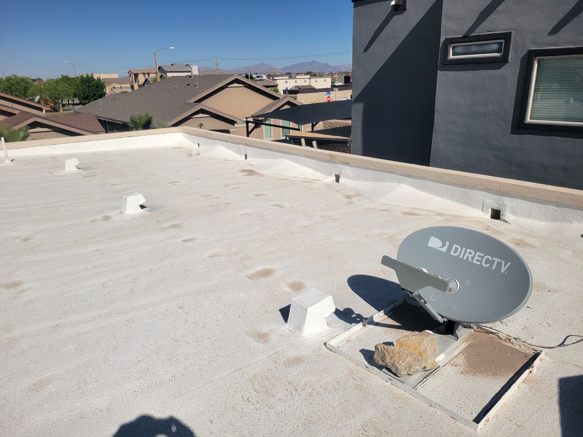 Rooftop with a DirecTV satellite dish beside a roof opening near a dark building wall.