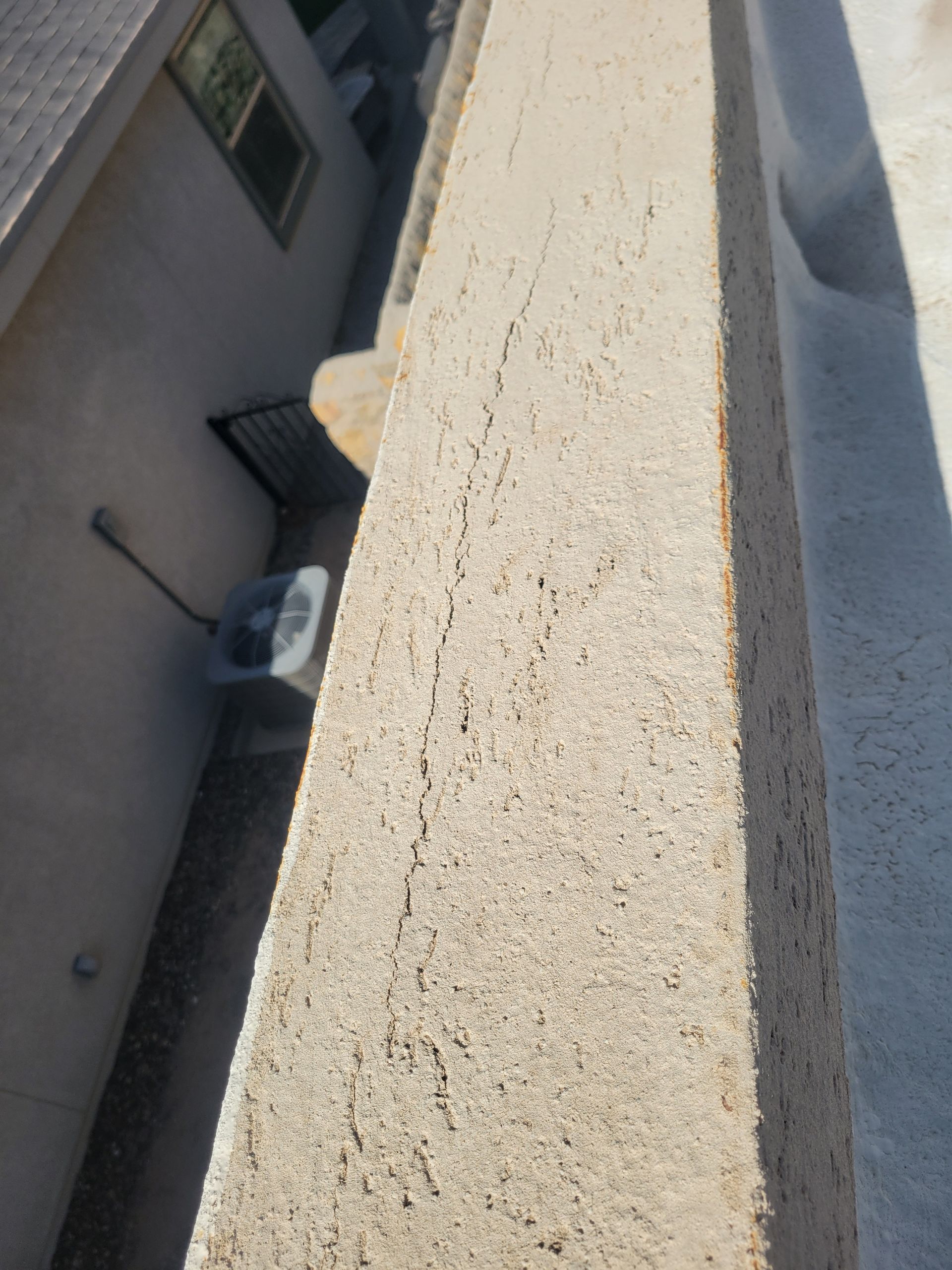 Tilted view of a beige stucco balcony ledge beside a building courtyard with windows and an HVAC unit below