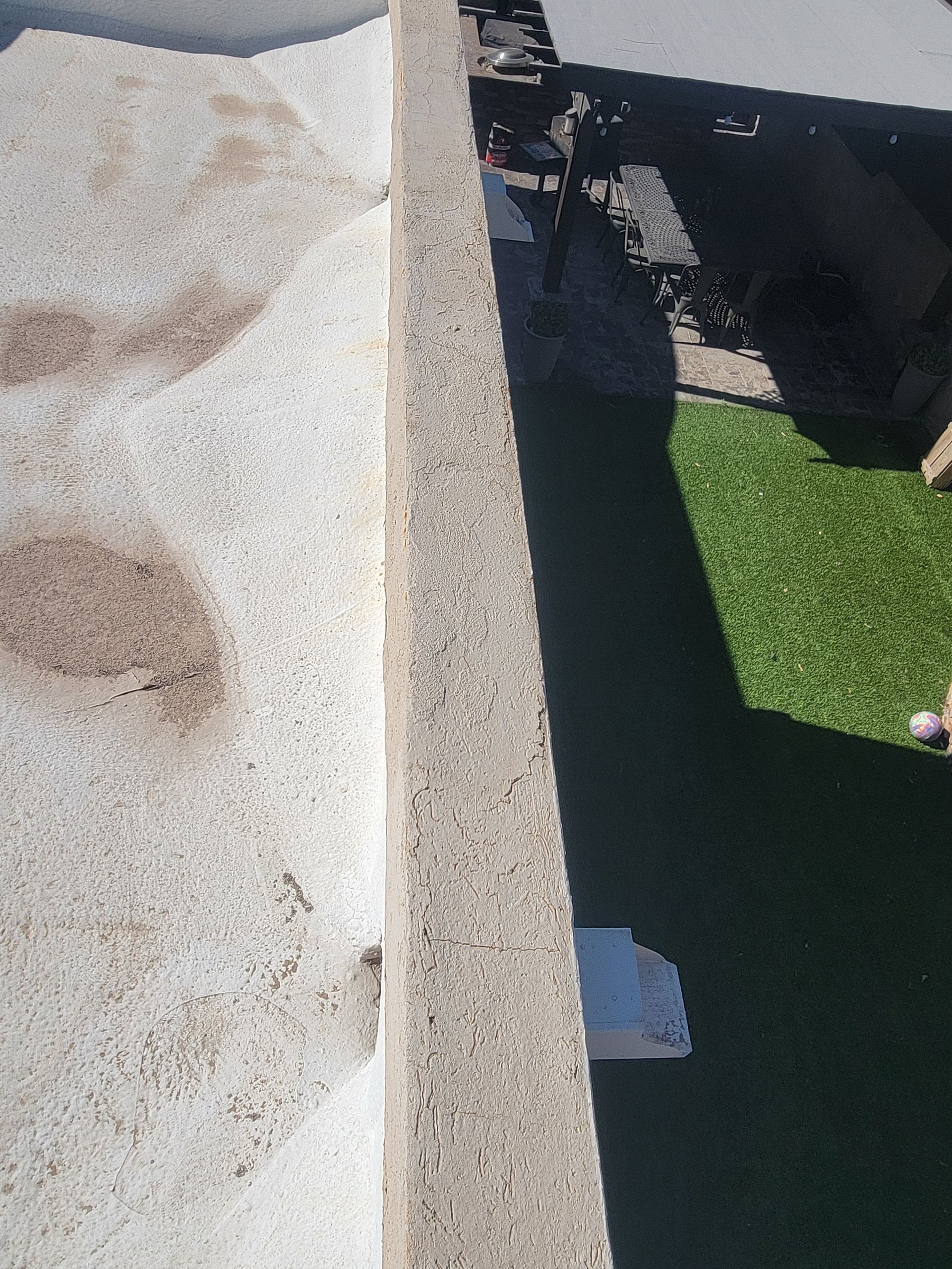 Rooftop ledge beside a dark yard with green artificial grass and a white chair below.