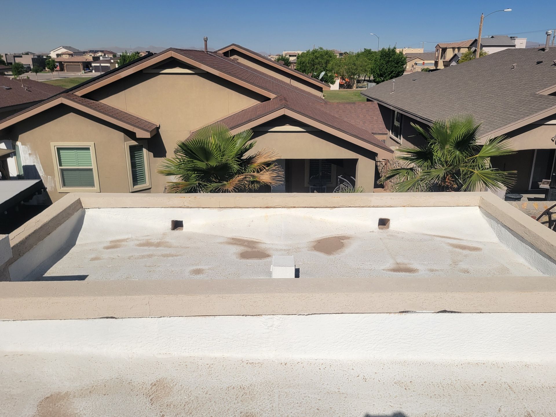 Rooftop view of suburban houses under a clear blue sky, with a flat white roof in the foreground