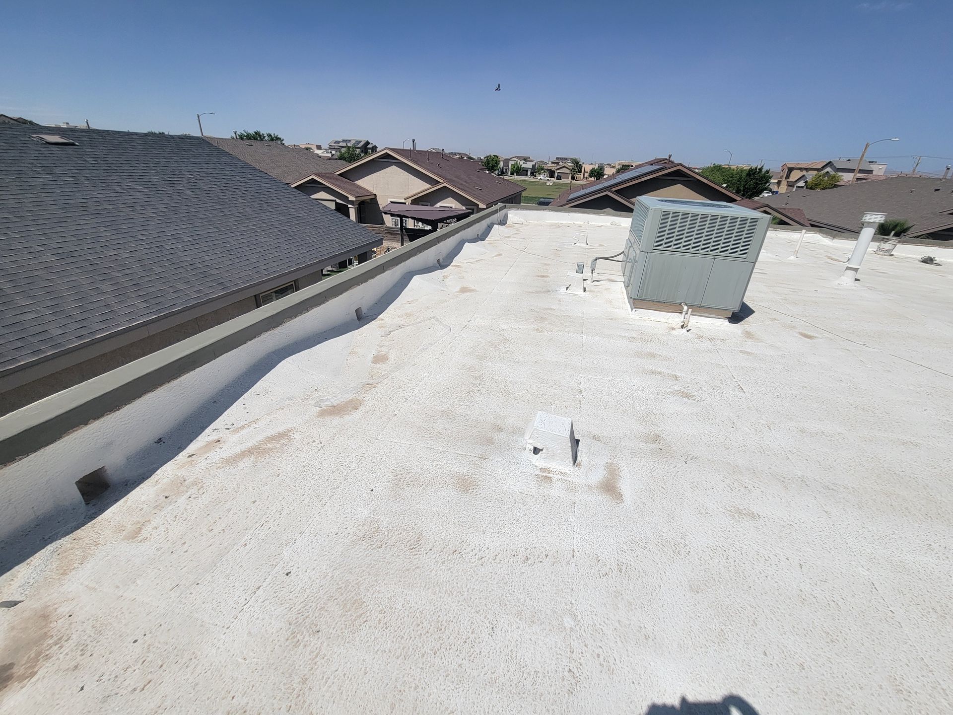 Flat white rooftop with HVAC unit, neighboring houses, and blue sky.