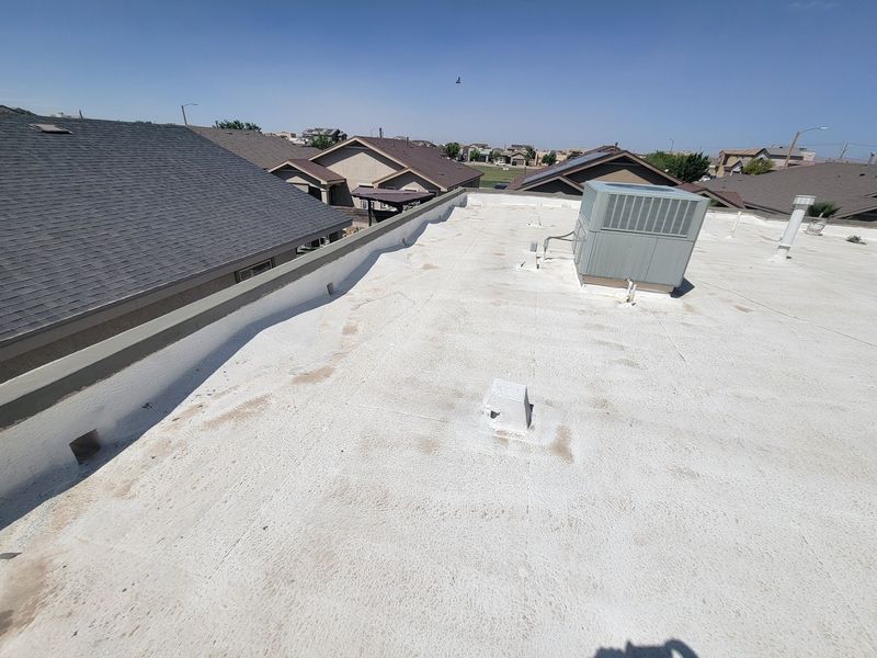 Flat white rooftop with HVAC unit, neighboring houses, and blue sky.