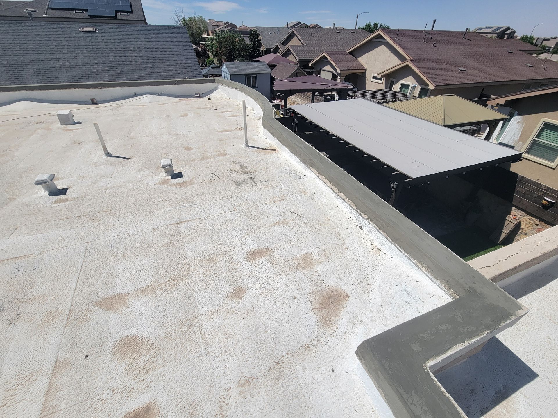 Flat white rooftop with vent pipes overlooking neighboring houses on a sunny day