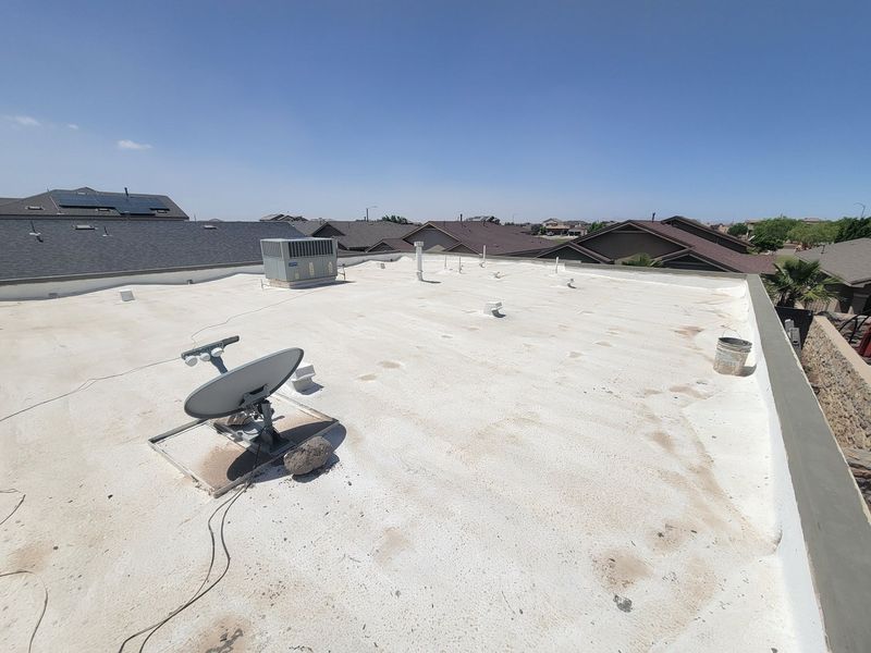 Rooftop with white coating, satellite dish, vents, and neighboring houses under a clear blue sky