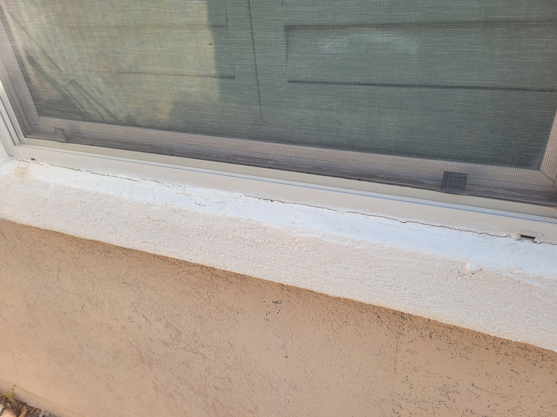 Close-up of a window screen and white sill above a beige stucco wall