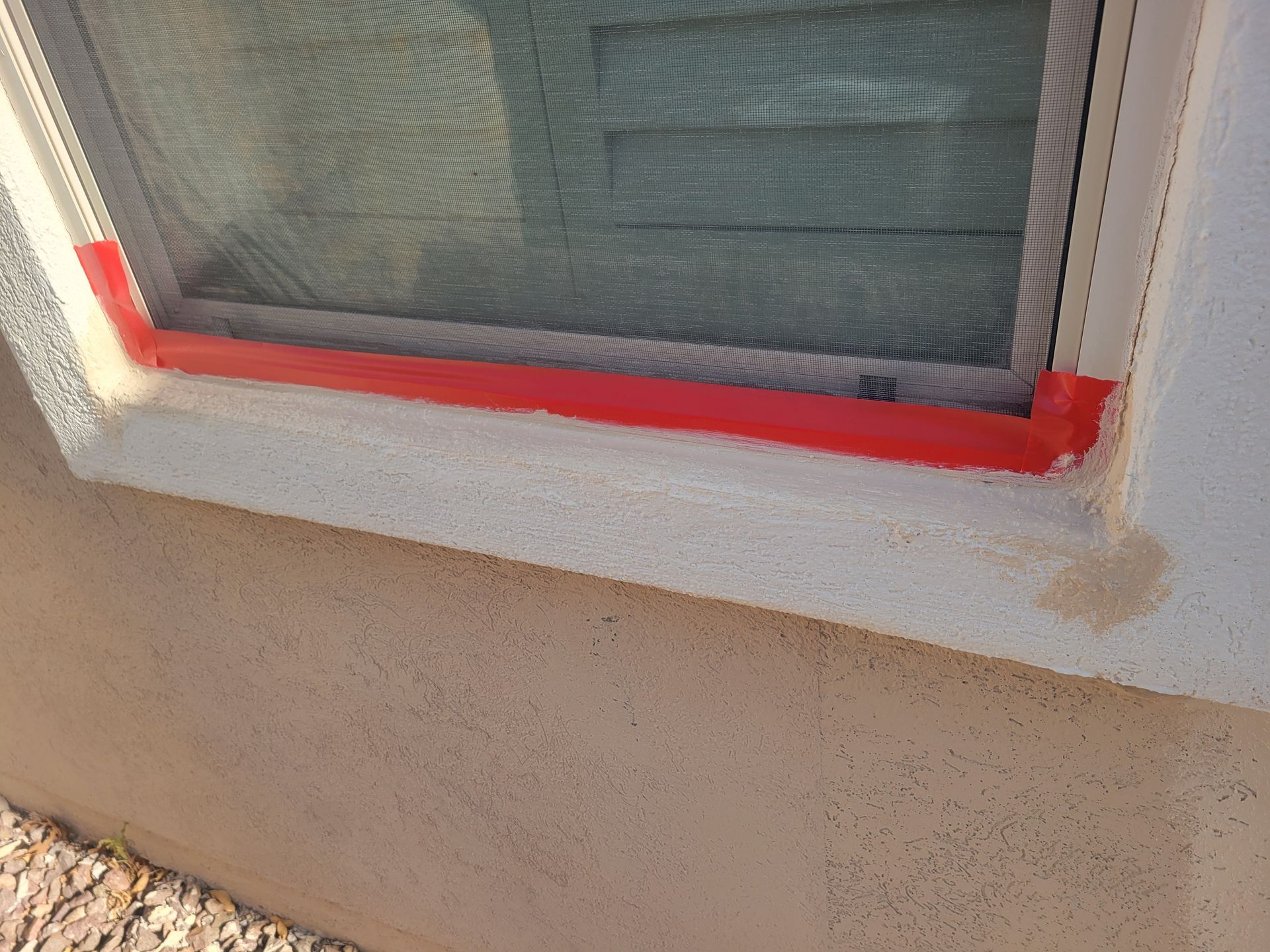 Close-up of a window with red-painted trim above a beige stucco wall