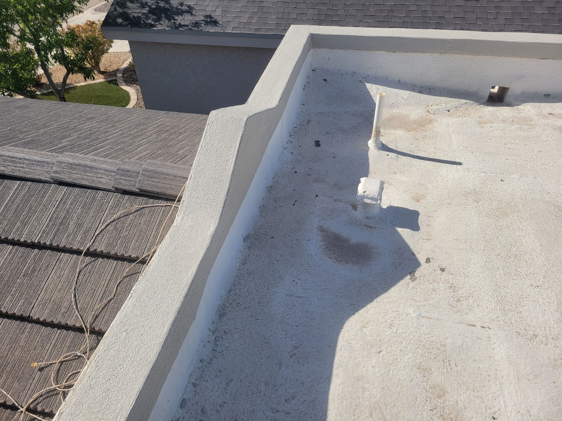 Flat rooftop with gravel and white roof coating near a parapet wall, viewed in sunlight