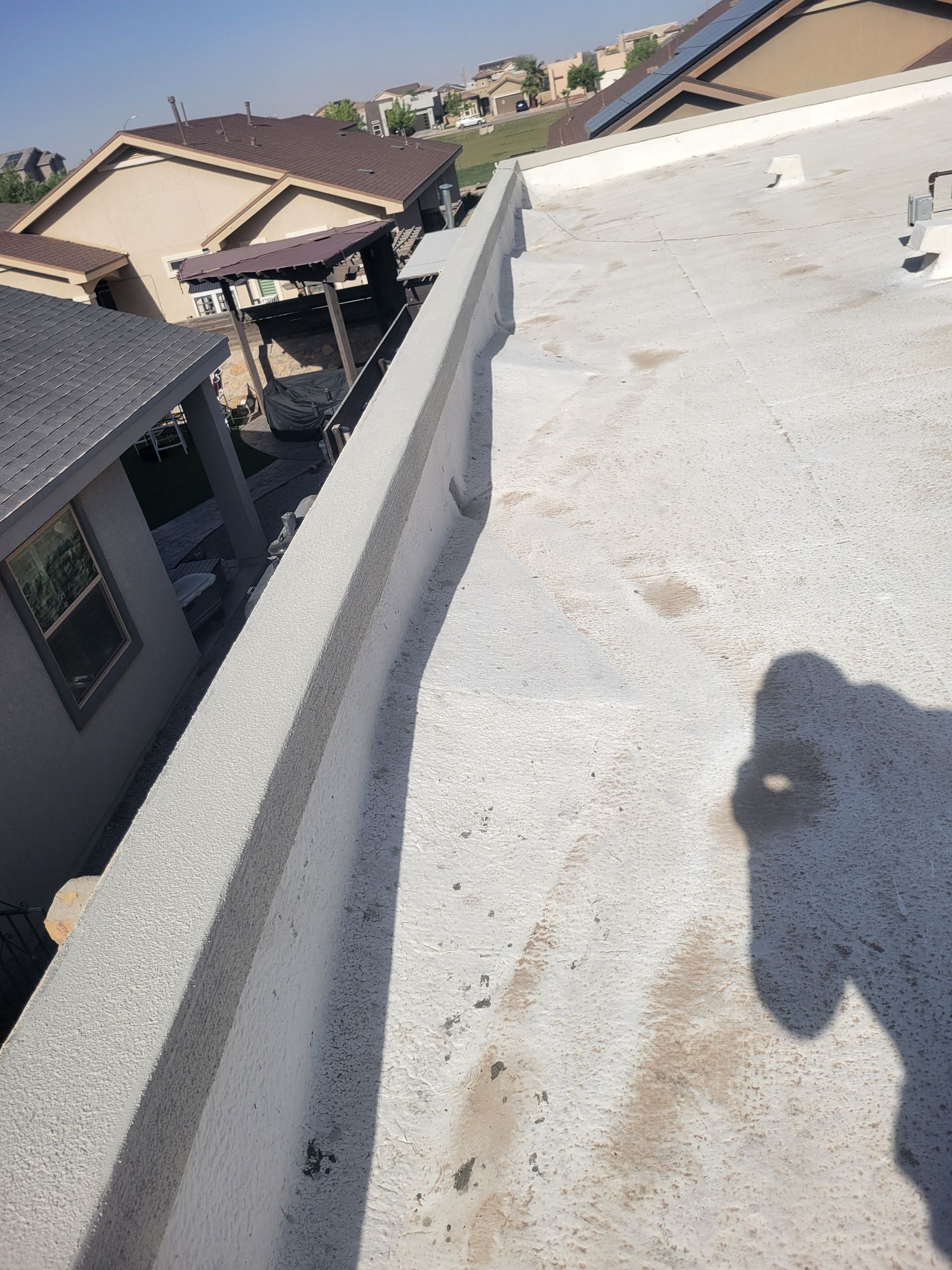 Rooftop with white parapet wall, neighboring houses, and a person’s shadow in bright sunlight
