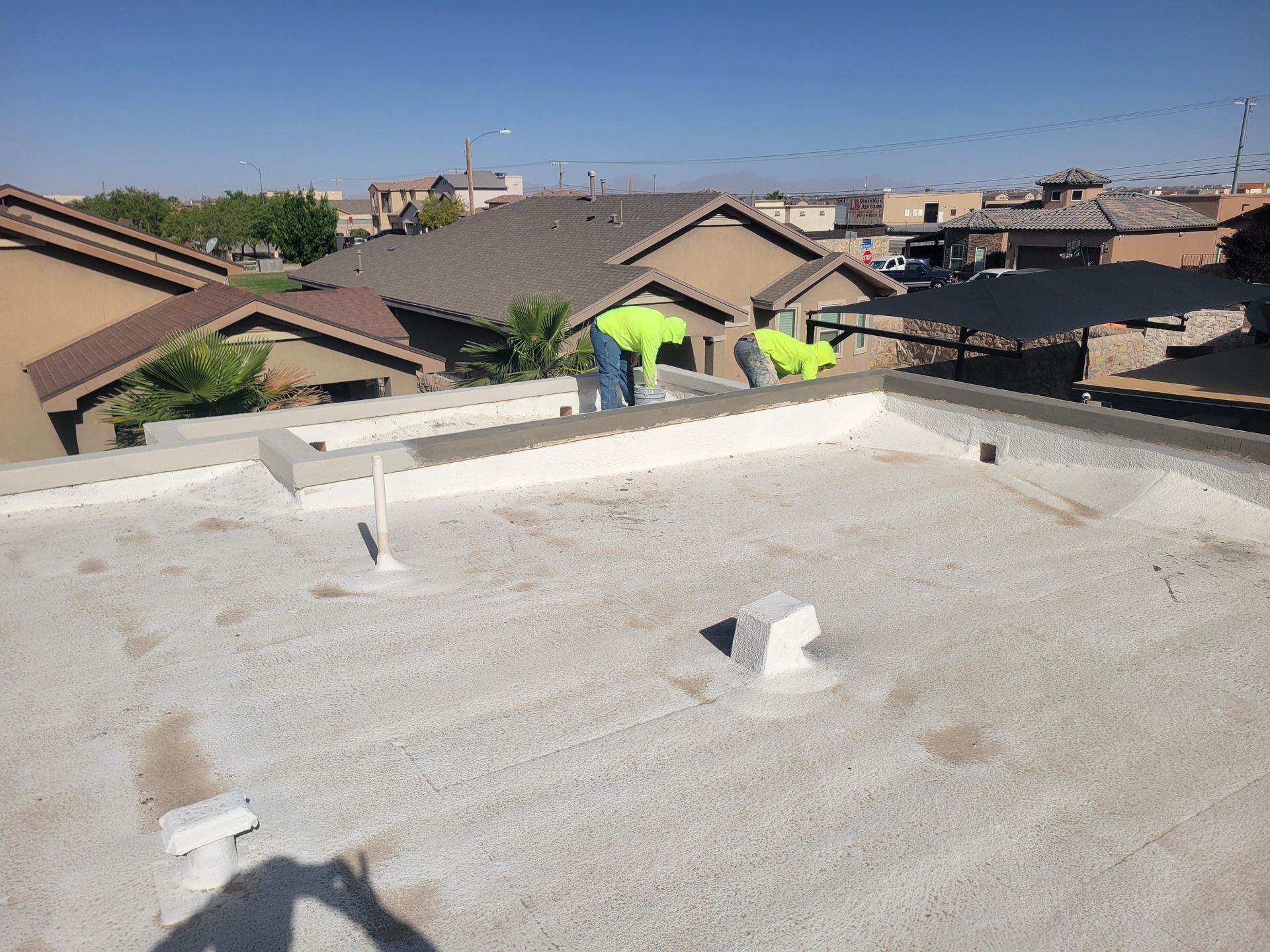 Rooftop with workers in neon safety vests on a residential roof under a clear blue sky